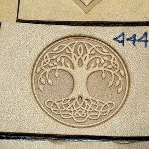 Puede incluir: Un sello de cuero marrón con una talla detallada de un diseño de árbol de la vida. El sello está etiquetado con el número "444".
