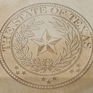 以下が含まれることがあります： 中央の星を囲む「THE STATE OF TEXAS」の文字が入った円形エンブレム。ベージュ色のエンブレムには、星、葉、小さな星の彫刻が施されており、質感のある外観になっています。デザインはおそらくスタンプまたはシールのためのものです。