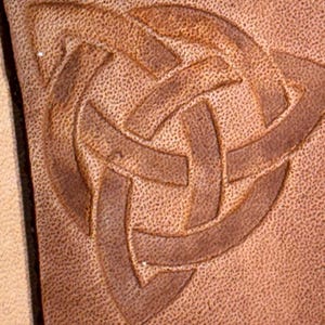 May include: A close-up of a brown leather patch with a detailed embossed Celtic knot design.