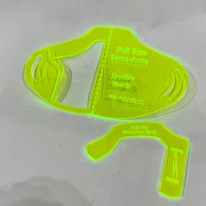 Puede incluir: Una plantilla de plástico amarillo brillante para hacer mascarillas. La plantilla está etiquetada como "Full Size Semi-Auto" y "Double Stack".