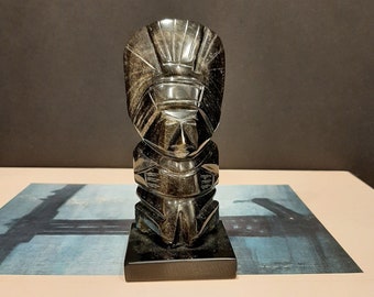 May include: A black obsidian sculpture of a stylized human figure with geometric features. The sculpture is on a black base and is about 6 inches tall.