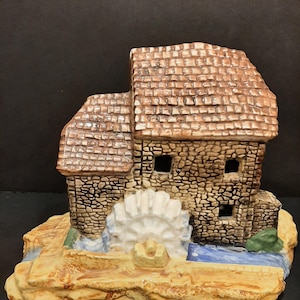 May include: A ceramic miniature model of a stone watermill with a brown tiled roof, a white water wheel, and a small stream. The model is painted in shades of brown, white, and blue.