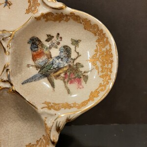 May include: A white ceramic serving dish with three sections. The dish is decorated with gold trim and a painted design of two birds on a branch with flowers.