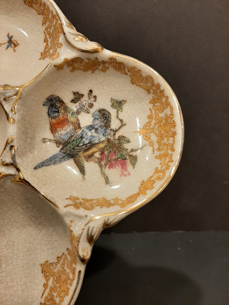 May include: A white ceramic serving dish with three sections. The dish is decorated with gold trim and a painted design of two birds on a branch with flowers.