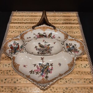 May include: A white porcelain serving dish with a gold rim and a floral design featuring birds. The dish has four sections and a handle.