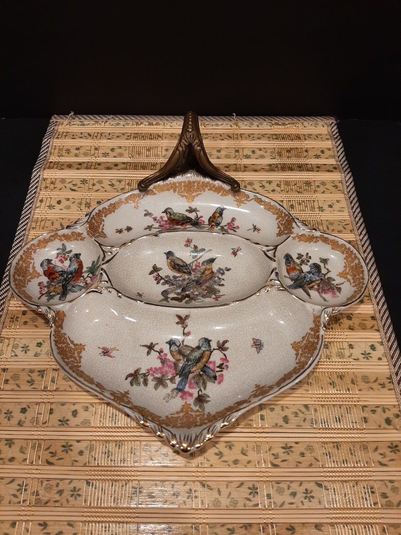 May include: A white porcelain serving dish with a gold rim and a floral design featuring birds. The dish has four sections and a handle.