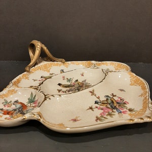 May include: A white ceramic serving tray with a gold rim and a gold handle. The tray is divided into four sections and features a floral design with birds.