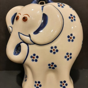 May include: A white ceramic elephant figurine with blue and brown floral patterns. The elephant has a hole in its head for hanging.