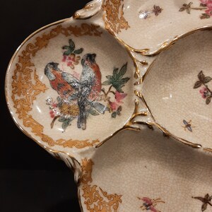 May include: A white ceramic serving dish with four sections. The dish is decorated with gold trim and floral designs, including two birds in the center section.