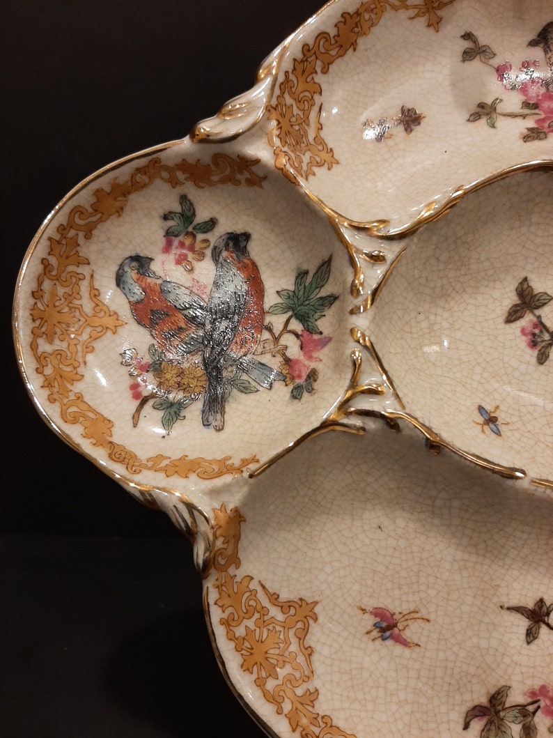 May include: A white ceramic serving dish with four sections. The dish is decorated with gold trim and floral designs, including two birds in the center section.