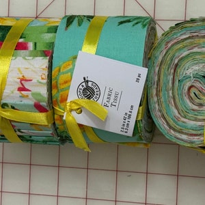 Może przedstawiać: Trzy rolki wzorzystej tkaniny, związane żółtą wstążką. Tkanina ma wzory owoców i tropikalne. Etykieta głosi "Fabric Tissu" i wymienia wymiary 6,3 cm x 106,6 cm. Do szycia.