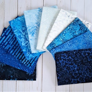 May include: A collection of ten blue and white fabric squares with various patterns, including floral, geometric, and abstract designs. The fabric squares are arranged in a fan shape on a white wooden surface.