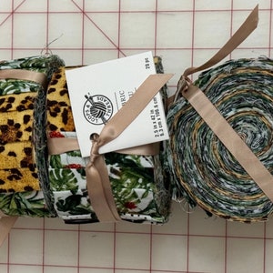 Puede incluir: Tres rollos de recortes de tela, cada uno atado con una cinta beige. Los recortes de tela son de varios patrones, incluyendo estampado de leopardo, floral verde y blanco, y un patrón geométrico verde y blanco. La etiqueta en el rollo del medio dice "Soybu Fabric 2.5 in x 42 in 23 pc 6.3 cm x 106.6 cm".