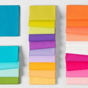 May include: A stack of 10 fabric squares in various shades of blue, green, and yellow. The fabric squares are arranged in a rainbow pattern.