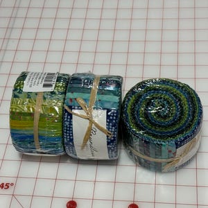 May include: Three rolls of fabric scraps in blue, green, and white patterns. The fabric is wrapped in plastic and tied with twine. The label on one roll reads "Boundless".