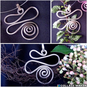 Könnte beinhalten: Eine silberne Drahtkette mit einem spiralförmigen Anhänger und einer strukturierten Oberfläche. Der Anhänger ist auf einem schwarzen Hintergrund und auf einem grünen Blatt-Hintergrund zu sehen.