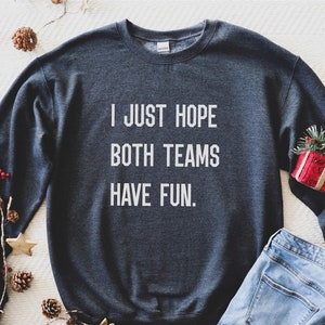 May include: A dark gray sweatshirt with the text "I JUST HOPE BOTH TEAMS HAVE FUN." printed in white.
