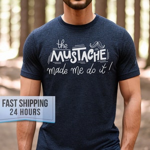 May include: Navy blue t-shirt with the text "the MUSTACHE made me do it!" in white. The shirt has a crew neck and short sleeves. The graphic includes a stylized mustache.