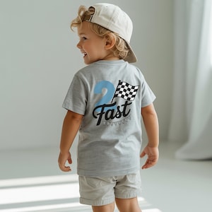 A young boy wearing a gray t-shirt with a checkered flag design and the text "Fast" on the back, smiling and looking away from the camera.