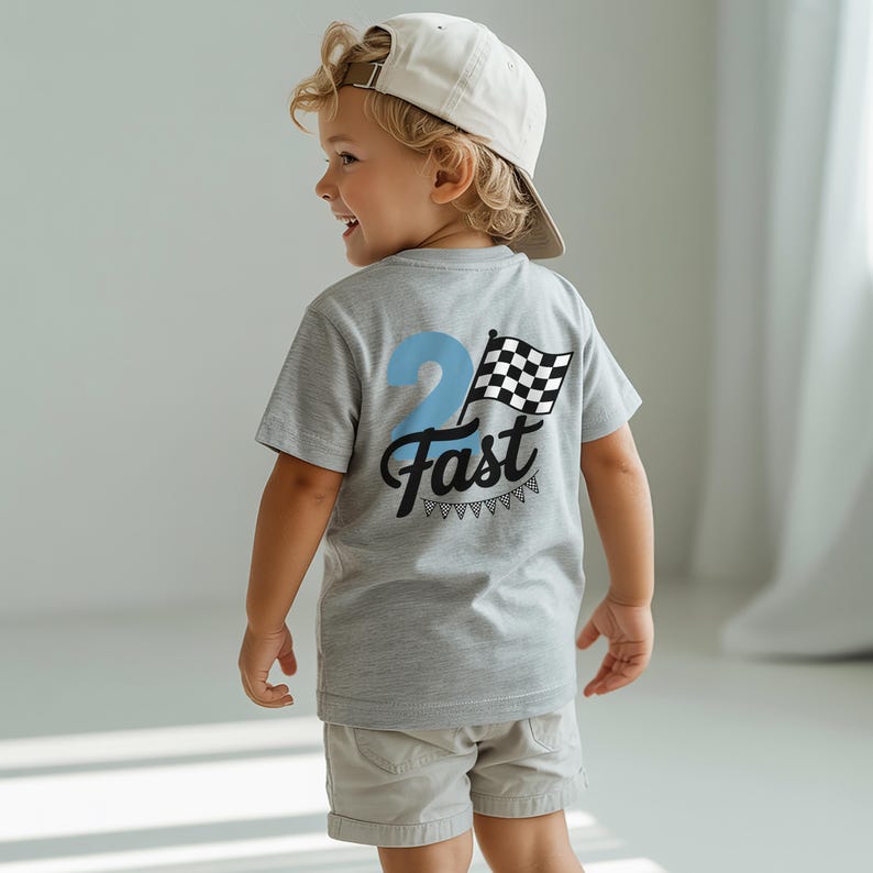 A young boy wearing a gray t-shirt with a checkered flag design and the text "Fast" on the back, smiling and looking away from the camera.