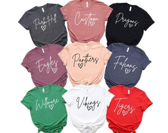 May include: A collection of nine short-sleeve crew neck t-shirts in various colors including dark gray, mauve, black, maroon, peach, navy, green, white, and red. Each shirt features a unique word and a heart graphic printed in a script font.