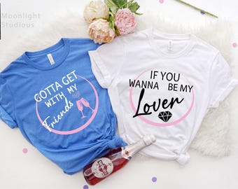 May include: A blue t-shirt with white text reading "GOTTA GET WITH MY Friends" and a white t-shirt with black text reading "IF YOU WANNA BE MY Lover" inside pink circles. Both shirts feature graphic icons of champagne flutes and a diamond.