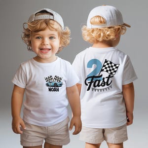 A smiling young boy wearing a white t-shirt with a race car design and the text "Noah 2 Fast" on the back.