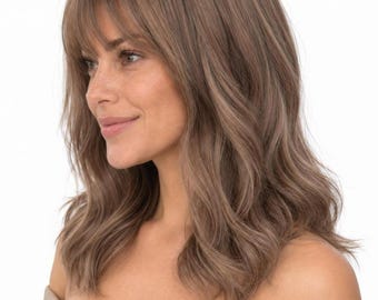 May include: A shoulder-length, light brown wig with soft, loose waves and straight-cut bangs that frame the forehead. The hair features subtle highlights and a natural-looking texture, styled to fall around the shoulders in a layered, wavy cut.