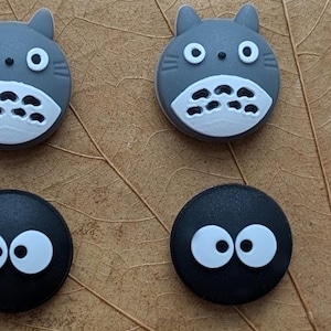 May include: Six round, colorful, cartoon character buttons with different facial expressions. The buttons are made of silicone and feature characters from the animated film, My Neighbor Totoro.
