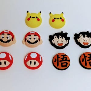 Könnte beinhalten: Eine Sammlung farbenfroher Accessoires mit Cartoon-Charakteren. Enthält gelbe Pikachu-Gesichter, Mario-Gesichter, rot-weiße Pilzdesigns und orangefarbene Kreise mit japanischen Schriftzeichen. Diese Accessoires sind wahrscheinlich für Schuhe oder andere Artikel.