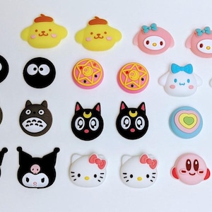 Puede incluir: Un conjunto de 18 cubiertas de botones de silicona de colores con temática de personajes. Las cubiertas presentan personajes de dibujos animados populares como Hello Kitty, Totoro y Sailor Moon.