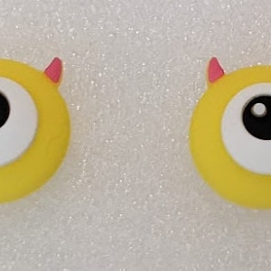 May include: Two yellow, one-eyed monster-shaped buttons with pink horns.