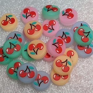 May include: Assortment of colorful cherry-themed resin buttons with various designs. The buttons feature red, pink, green, yellow, and white cherries on a variety of colored backgrounds.
