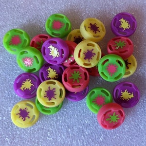 May include: A collection of colorful silicone controller caps for gaming consoles. The caps feature a variety of bright colors, including green, yellow, purple, and pink, with a splatter paint design.