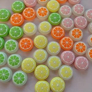 May include: Assortment of colorful round buttons with various fruit designs, including lemons, limes, oranges, and pineapples. The buttons are made of a smooth, glossy material and have a raised design.
