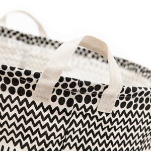 May include: A black and white patterned fabric laundry basket with two white fabric handles. The pattern features black polka dots and a black and white zig zag design.