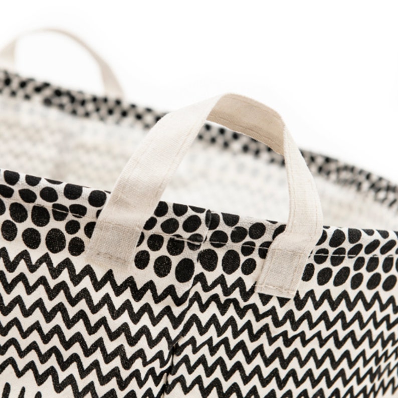 May include: A black and white patterned fabric laundry basket with two white fabric handles. The pattern features black polka dots and a black and white zig zag design.