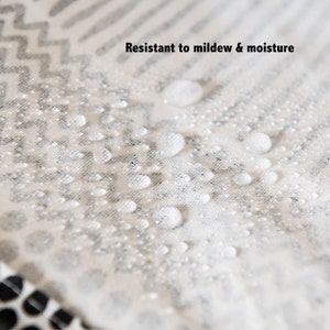 May include: Close-up of a white fabric with a black and white geometric pattern. Water droplets are on the fabric, demonstrating its resistance to mildew and moisture.