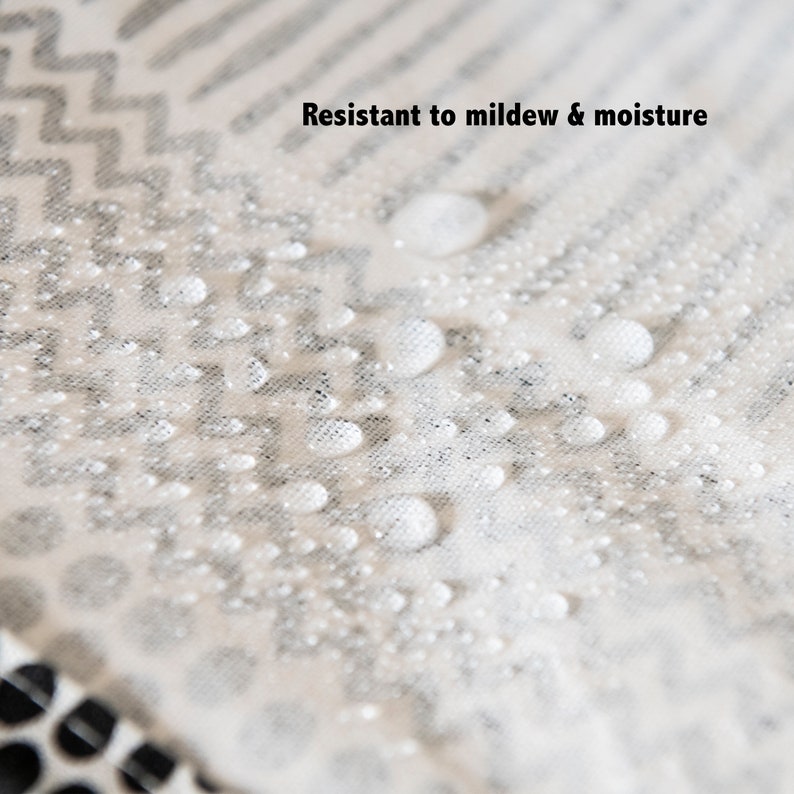 May include: Close-up of a white fabric with a black and white geometric pattern. Water droplets are on the fabric, demonstrating its resistance to mildew and moisture.