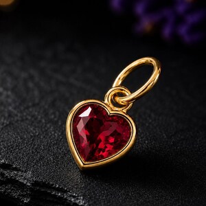 May include: A heart-shaped pendant featuring a deep red faceted gemstone set in a polished gold-toned metal frame. The pendant includes a small circular gold-toned jump ring attached to the top, designed for easy connection to a chain or necklace.