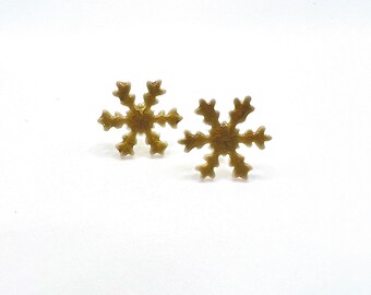 May include: A pair of gold-colored snowflake stud earrings. Each earring features a six-pointed design with intricate details, perfect for winter or holiday wear. The earrings are set against a white background.