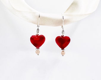 May include: A pair of heart-shaped earrings. Each earring features a glossy red heart pendant, a small silver bead, and a pale pink bead. The earrings hang from silver-colored ear wires. The background is white.