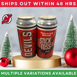 May include: Two red and silver beer can candles with the text "DEVILS" and "STICK TOSS" on them. The candles are on a gold stand, with Christmas ornaments and trees. The image also includes the text "MULTIPLE VARIATIONS AVAILABLE".