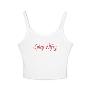 May include: A white sleeveless crop top with thin shoulder straps and a scoop neckline. The text Spicy Wifey is printed in red cursive script across the center of the chest. The garment is plain white with no other patterns or visible features.