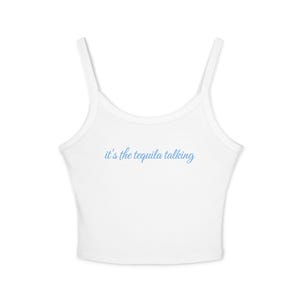 May include: A white sleeveless crop top with thin shoulder straps and a scoop neckline. The text "it's the tequila talking" is printed in a light blue cursive script across the center of the chest area on the front of the garment.