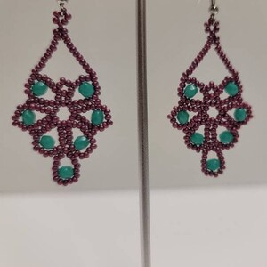 May include: A pair of dangle earrings with a geometric design. The earrings are made with maroon and teal beads.