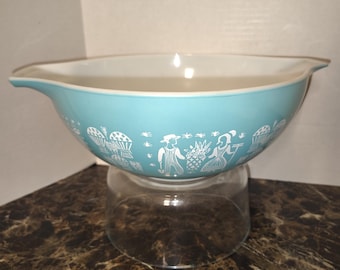 Peut inclure: Un bol mélangeur bleu clair avec un intérieur blanc et un motif graphique blanc sur l'extérieur. Le motif présente des illustrations répétitives de personnages portant des chapeaux, des paniers de produits et des éléments agricoles. Le bol a deux becs verseurs.