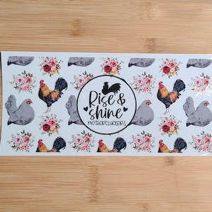 May include: A white background with a repeating pattern of gray chickens, red and pink floral bouquets, and a black and white circle with the text "Rise & shine Mothercluckers".