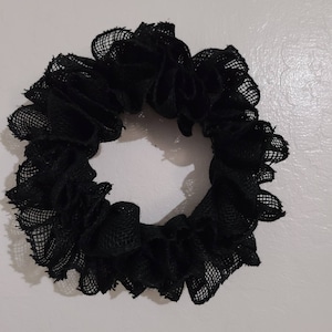 K&ouml;nnte beinhalten: Ein schwarzes Haargummi aus ger&uuml;schtem, netzartigem Stoff. Das Haargummi ist kreisf&ouml;rmig und scheint handgefertigt zu sein. Die dunkle Farbe und Textur deuten auf eine gotische oder kantige &Auml;sthetik hin, die f&uuml;r verschiedene Frisuren geeignet ist.