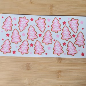 May include: A sheet of pink and white Christmas tree stickers with red stars. The stickers are perfect for decorating gifts, cards, or any other craft project.